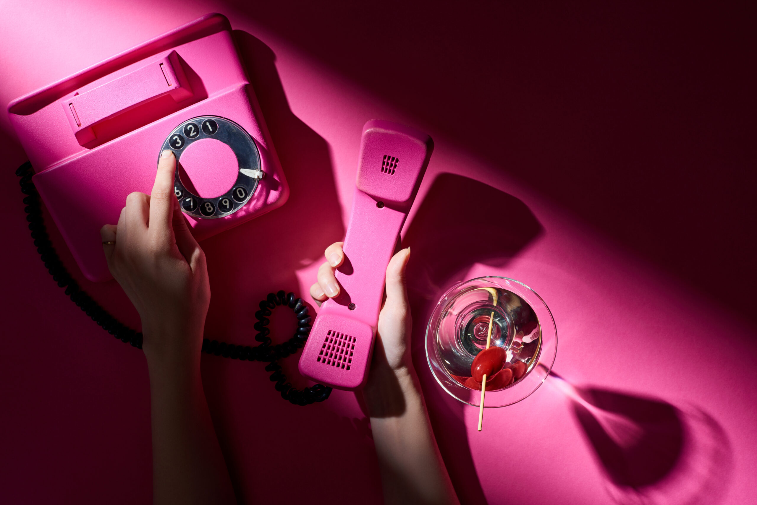 Cropped view of woman using vintage telephone beside cocktail on pink background